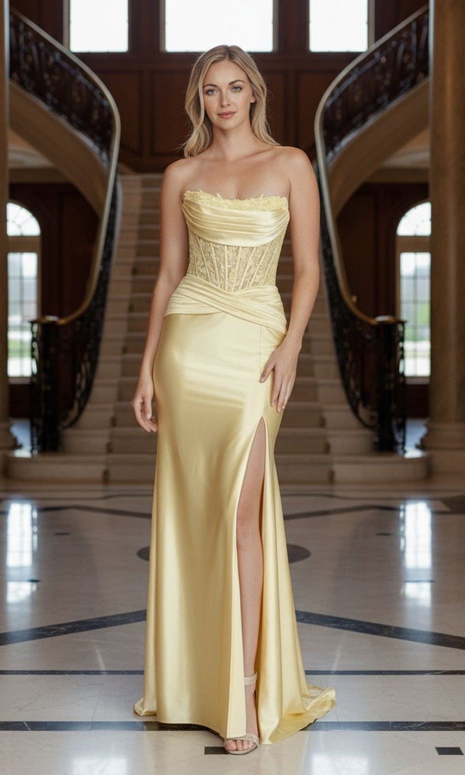 A woman in the Poly USA 25056 long yellow prom dress, featuring a strapless lace corset bodice and thigh-high slit, stands in a grand foyer with a staircase behind her.